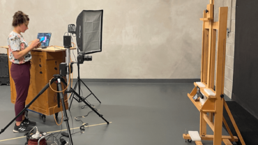 Studio with an easel, lights, a camera and a woman setting up the equipment.