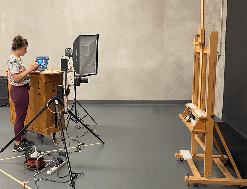 Studio with an easel, lights, a camera and a woman setting up the equipment.