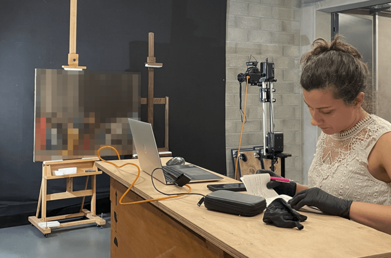 A woman reading notes in a room with a painting mounted on an easel during a photographic session.